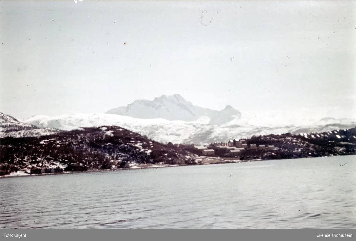 Skjomtinden, "Sovande Dronning", i Narvik kommune, sett fra sjøen. I forgrunnen ned mot sjøen ligger endel bebyggelse. 