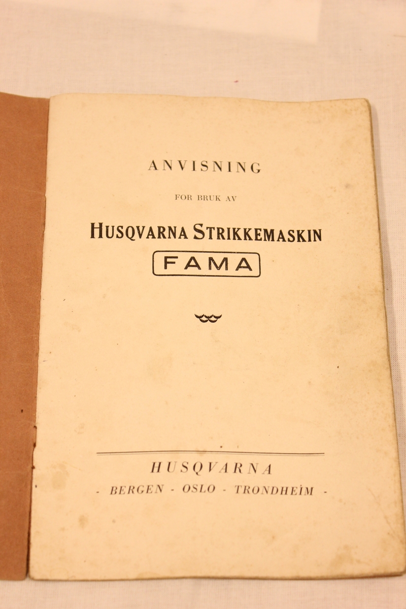 Strikkemaskin av merket "Husqvarna FAMA med femtråder ringelapparat" på understell i tre. Det er følger med diverse ekstra nye nåler(bilde 10 og 11), bruksanvisning(bilde5) Inne i boken står det "Helsingborg 1935. Schmidts Boktryckeri A.-B 1549 osv.