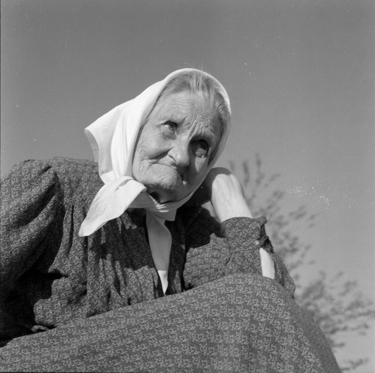 Elisabeth i Karvala, en eldre kvinne med skaut og kjole, sitter og lener hodet på armen.