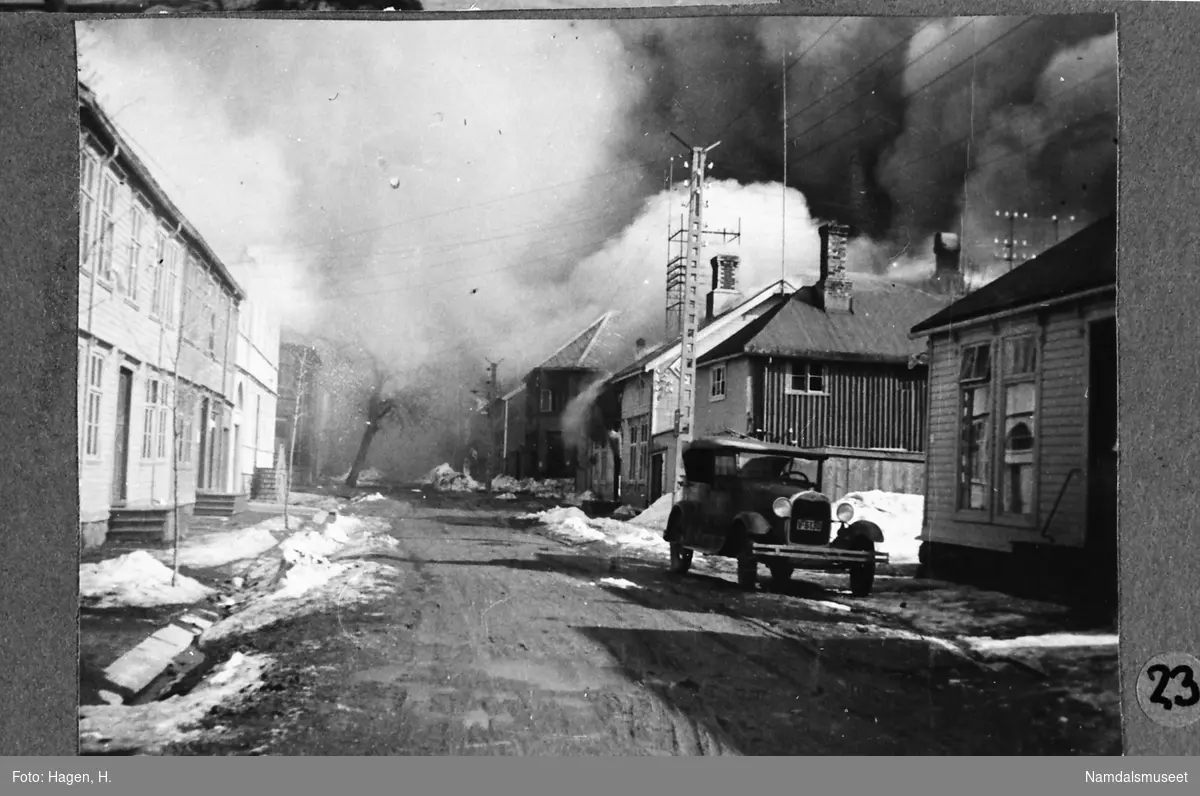 Namsos sentrum, 20.04.1940. "Nora-hjørnet" står i flammer. I forgrunnen en personbil ant. nr. V-6130.