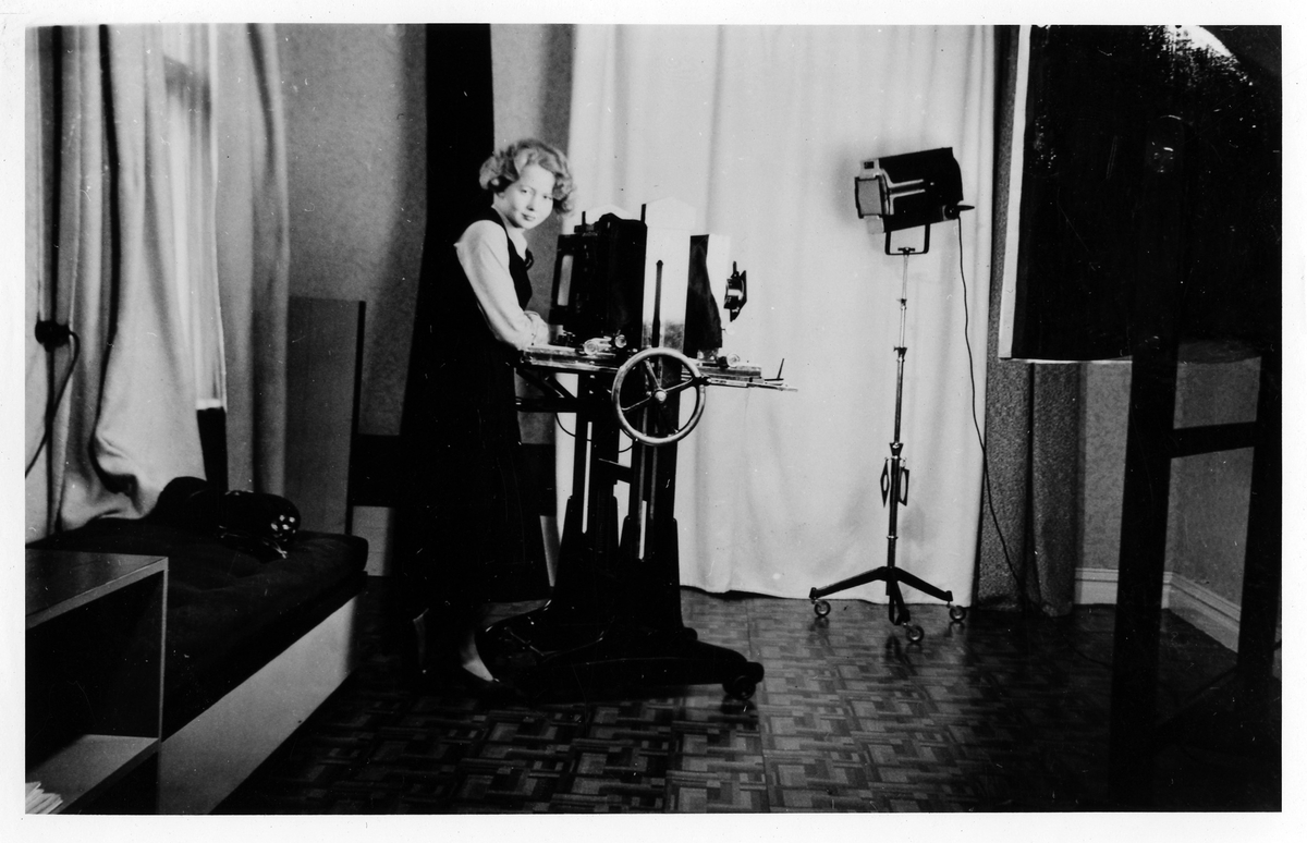 En kvinna, troligen Hildur Thorssin-Larsson, står framför en kamera i Thorssin-Larssons fotoateljé.