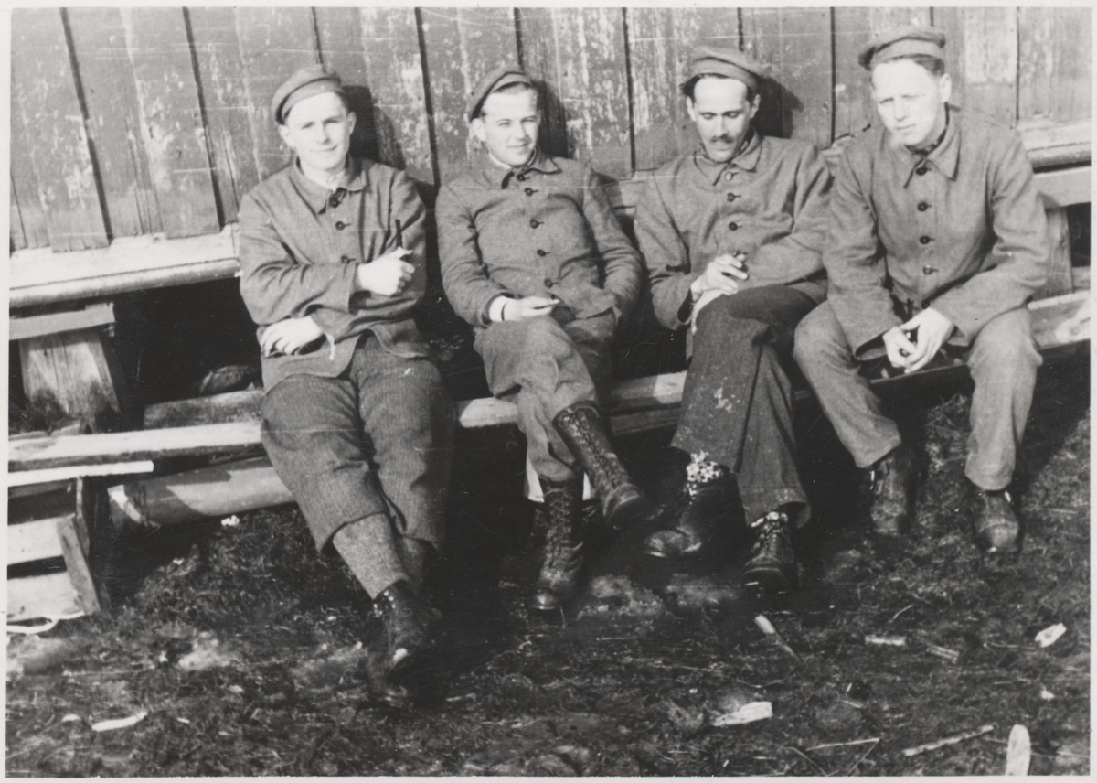 Gruppe av "Trondheimsgislene" på Falstad våren 1942. Fra venstre Arne Fjellbu jr., Per Jahn Kiønig, Viggo Bredal Hansen (Heirung) og John Arnstad. Bildet er tatt på Falstad nedre, ved stabburet på vestsida av driftsbygningen.