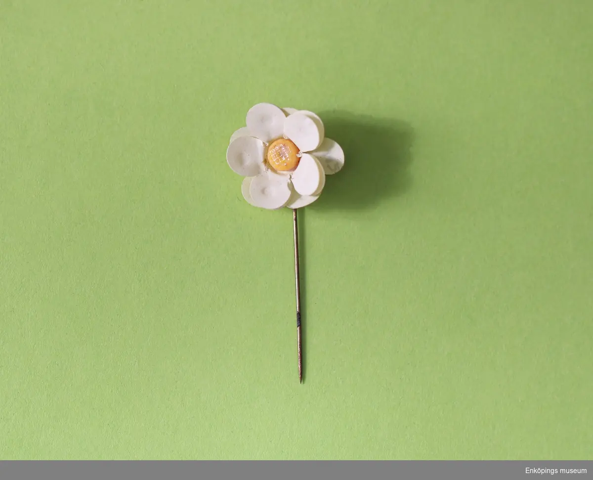 Majblomma från 1926.
Blomman är gjord av vit celluloid och har fem blad i 3 lager, totalt 15 blad och en gul mittknapp, även denna gjord av celluloid.
Det som håller blomman samman är en nål av mässing.