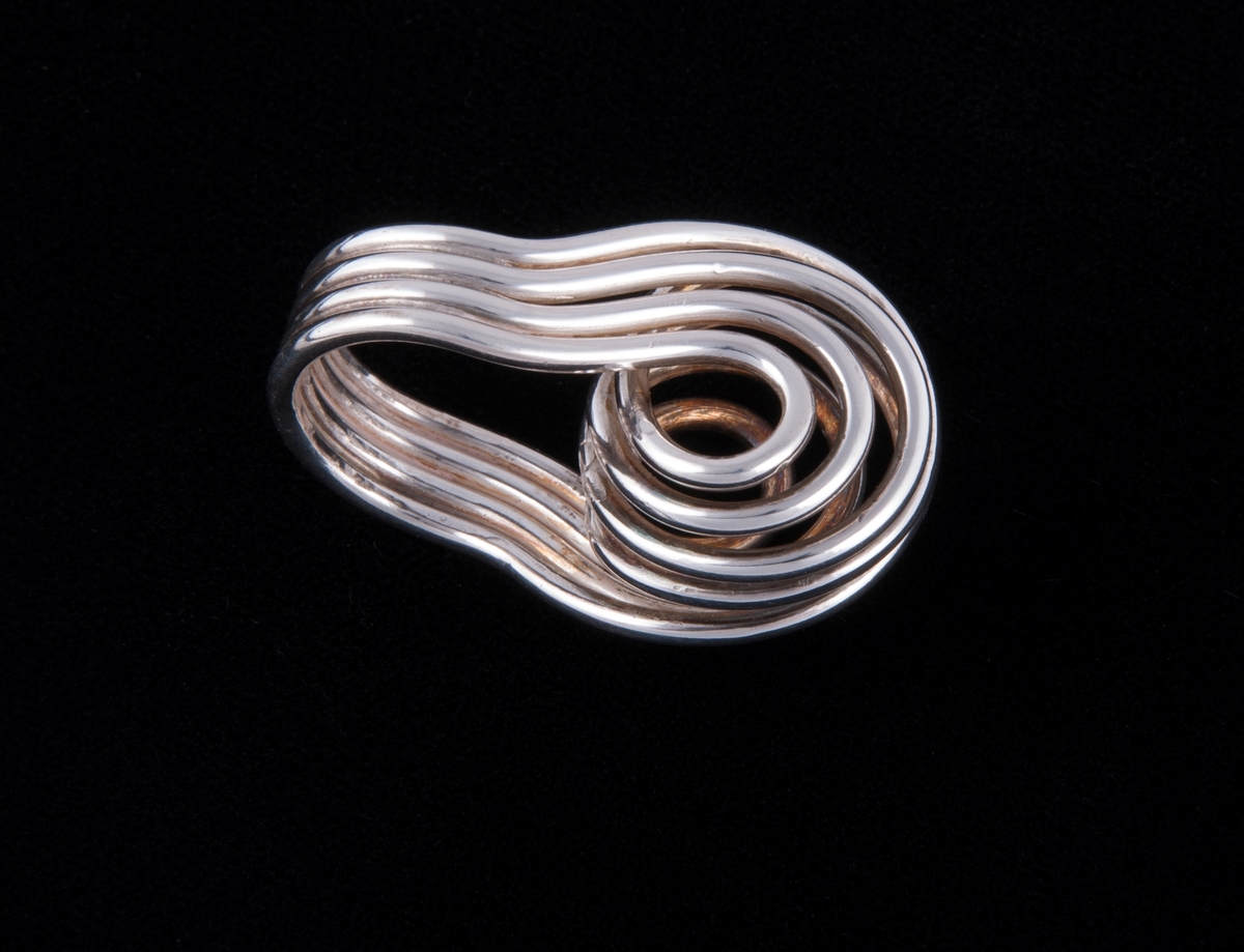 Sammensatt av fire sølvringer som er lagt parallelt til et bånd og vridd i en høy, kuleformet spiral på oversiden.