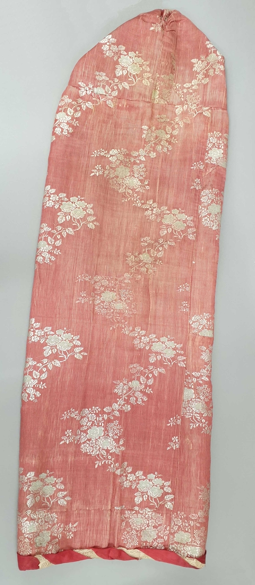 Dåpsveip av rosa silke, med innvevde hvite blomster. Fôr av mønstret bomullstoff. Tvinnet silkebånd og blondesløyfe langs kantene. Silkesløyfer med striper i flere farger, som knyttes foran.