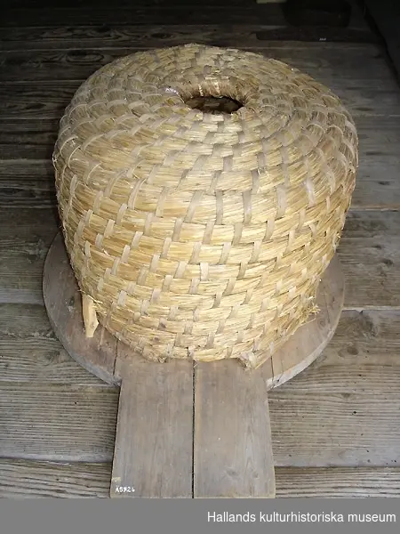 Bikupa med tillhörande bottenplatta i trä och en bikupehatt i trä, svarvad. Måtten på hatten är 90mm i diameter och 50mm i höjd.