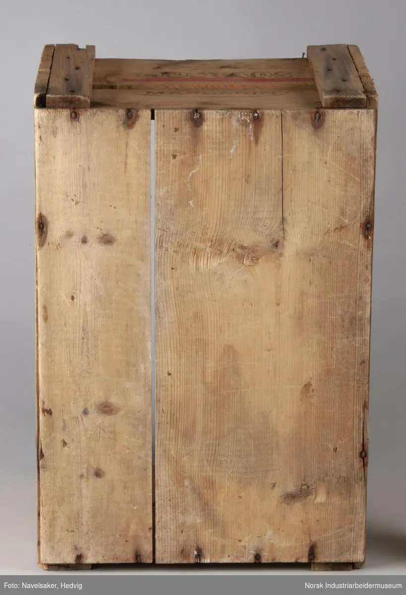 Trekasse fra O. Mustad & Søn for margarin. Kassen består av to plank på hver side. I kortsiden er plankene festet 1,5 cm på innsiden av plankene på langisden. Plankene er festet i hvert hjørne via en vertikal planke med spiker.