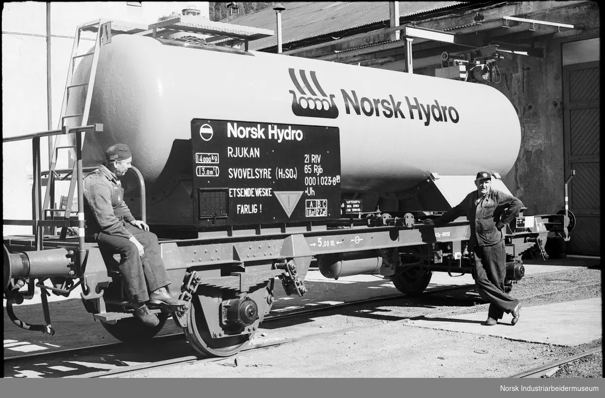 Arbeidere foran tankvogn på skinnegangen med logoen til Norsk Hydro på.
