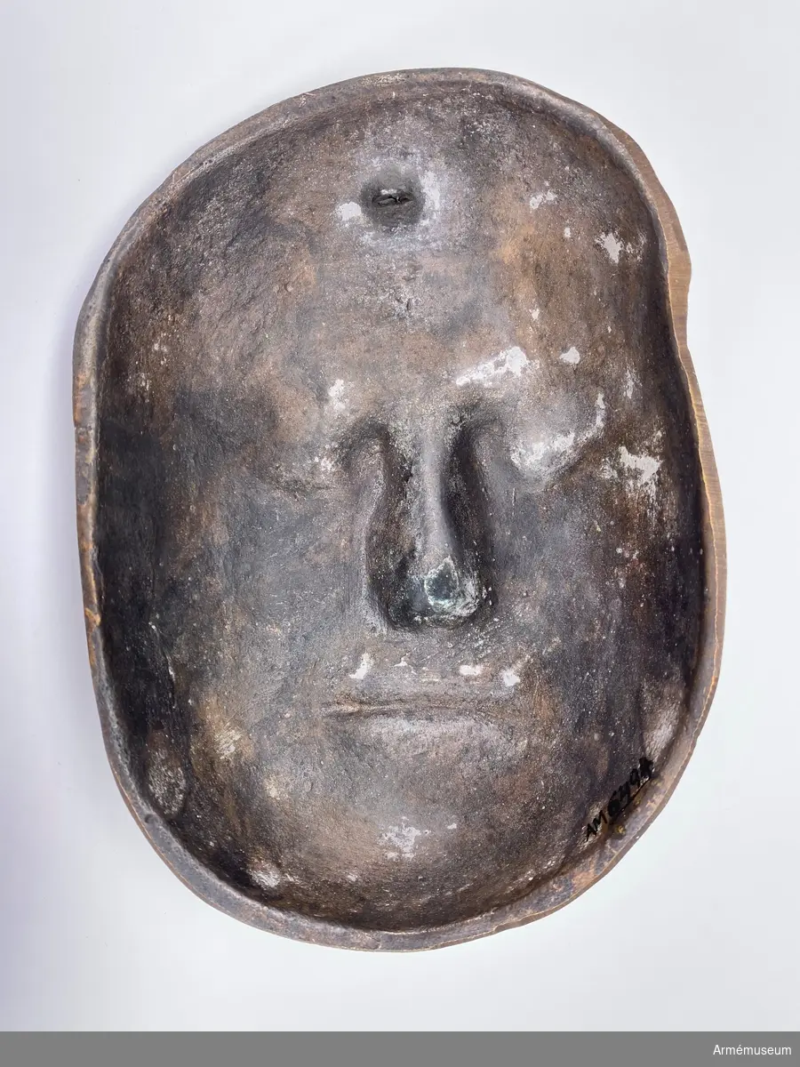 Bronsmask föreställande den döde Karl XII.

Enl styresman Olle Cederlöfs anteckningar med anledning av gåva AM.066063 (AM 73/475) är detta inte en dödsmask. 

"Proportionerna i ansiktet stämmer inte med kraniets proportioner enl 1918 års gravöppning - utan en av den schweiziske medaljgravören Hedlinger gjord frihandsmodellering inför konungens lik på Karlberg 1718. Hedlingers modell nu endast avsedd att ligga till grund för hans uppdrag: Att modellera en reliefbild för konungens mynt och minnespenningar. Hedlinger anlände till Sverige 1718-. Konungen hade då avlidit och Hedlinger hade aldrig sett Karl XII i levande livet, han tog chansen att fånga konungens ansikte inför 'lit de parade' på Karlberg. Hedlingers 'dödsmask' har senare avgjutits i gips, brons och  järn i olika sammanhang."