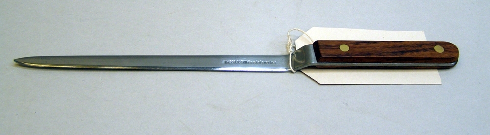 Brevkniven vinklad framför skaftet.
Skaftet har två plattor av ädelträ som är fästade med 2 mässingsnitar.