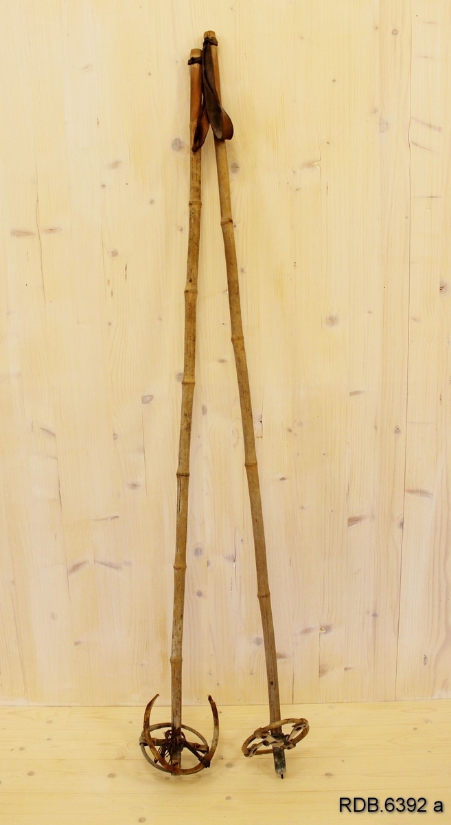 Et par eldre bambusstaver med brune lærstropper. Disse er tredd gjennom et hull øverst på staven. Stavene er påsatt nyere trinser, men på den ene staven er det rester av opprinnelig trinse som er festet med ståltråd.