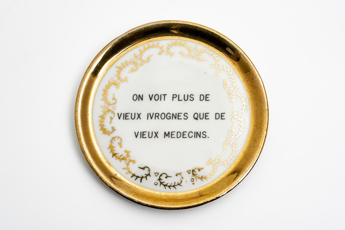 Glassbrikke i glasert keramikk med påskriften "On voit plus de vieux ivrognes que de vieux medecins." ("Man ser flere gamle drankere enn gamle leger"; fransk ordtak.)