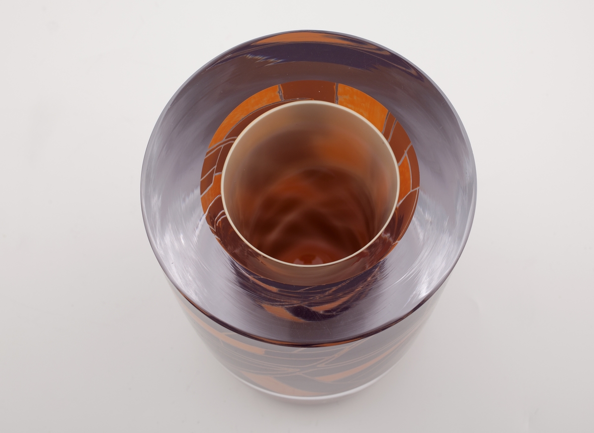 Massiv sylinderformet vase i underfangsglass, bestående av sjikt i melkehvitt, klart, samt opakt oransje- og sortfarget glass. Det sistnevnte sjiktet er delvis fjernet, slik at det melkehvite laget kommer til syne i form av geometriske linjeføringer. Planslipt topp og sirkulær åpning.