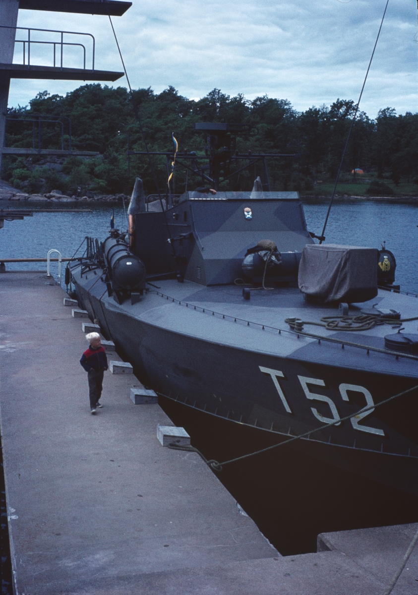 Bilden visar motortorpedbåten T 52 som ligger förtöjt på en brygga. På bryggan går ett barn och beskådar båten.