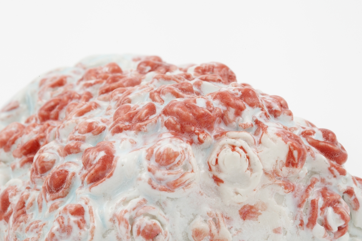 Lyseblå porselenskopp dekorert med røde prikker. Konvekse bobler utgjør koppens overflatestruktur, hvor boblene er rødglaserte og danner et dekorativt mønster som kan minne om roser. Koppen har to tynne hanker plassert tett sammen.