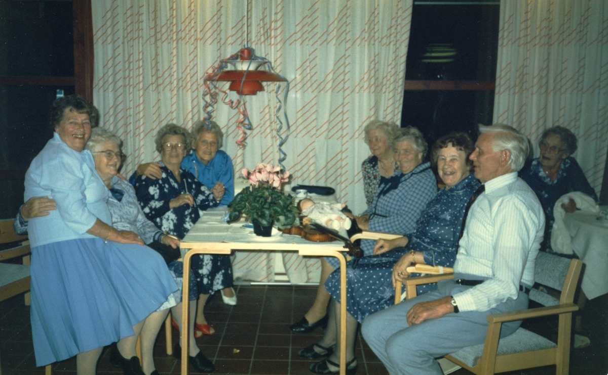 Samkväm på Brattåsgården cirka 1985 - 1990. Från vänster: 1. och 2. okända kvinnor, 3. Gurli Ekman (i mörk klänning), 4. Margit Antonsson (i blå blus), 5. Gerda Mattsson (vid fönstret), 6 Sigrid Olsson, 7. Maria Brattberg, 8. okänd man i ljus skjorta, 9. Elin Jansson.