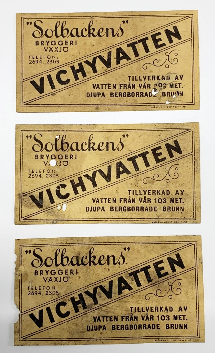 Tre stycken identiska etiketter: "Solbackens" // BRYGGERI // VÄXJÖ // VICHYVATTEN // TILLVERKAD AV // VATTEN FRÅN VÅR 103 MET. // DJUPA BERGBORRADE BRUNN"
