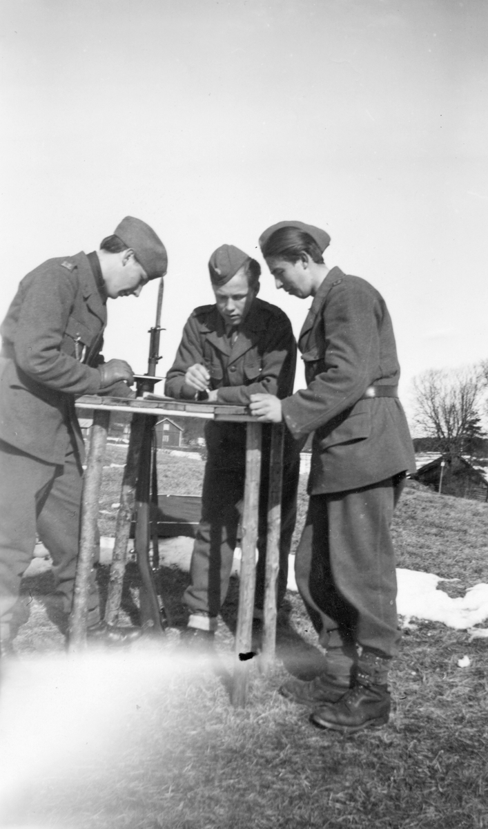 Tre frivilliga luftbevakare tillhörande landstormsregemente L 2 läser karta. Iklädda uniform. I Dalsland under beredskapstiden.