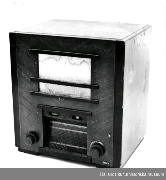 Radioapparat av märket Dux Typ U75. Uttag för grammofon. Lik- och växel-ström. Fronthögtalare, tygklädd högtalaröppning. Mångkantiga knappar.Rikliga stationsmarkeringar.Bredd: 40 cm.Djup: 31cm.Höjd: 44 cm. 