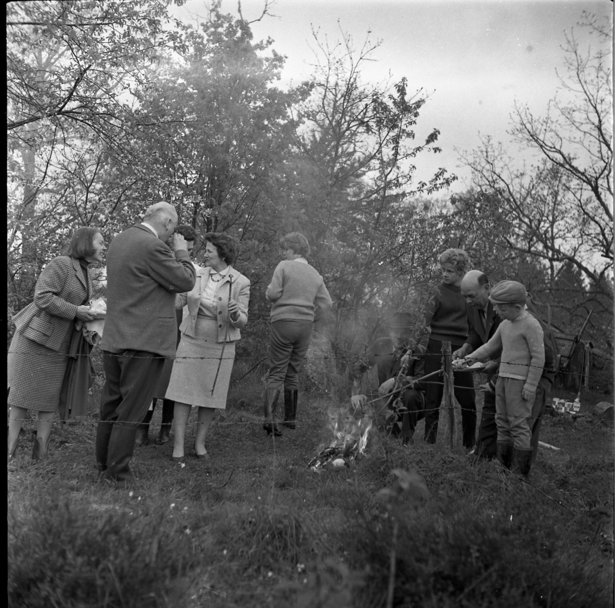Barn och vuxna samlade runt en eld för korvgrillning. Det är gökotta, möjligen i Gränna Lions regi. Mannen till vänster är Sture Petri, till höger om honom står Margit Antonsson.