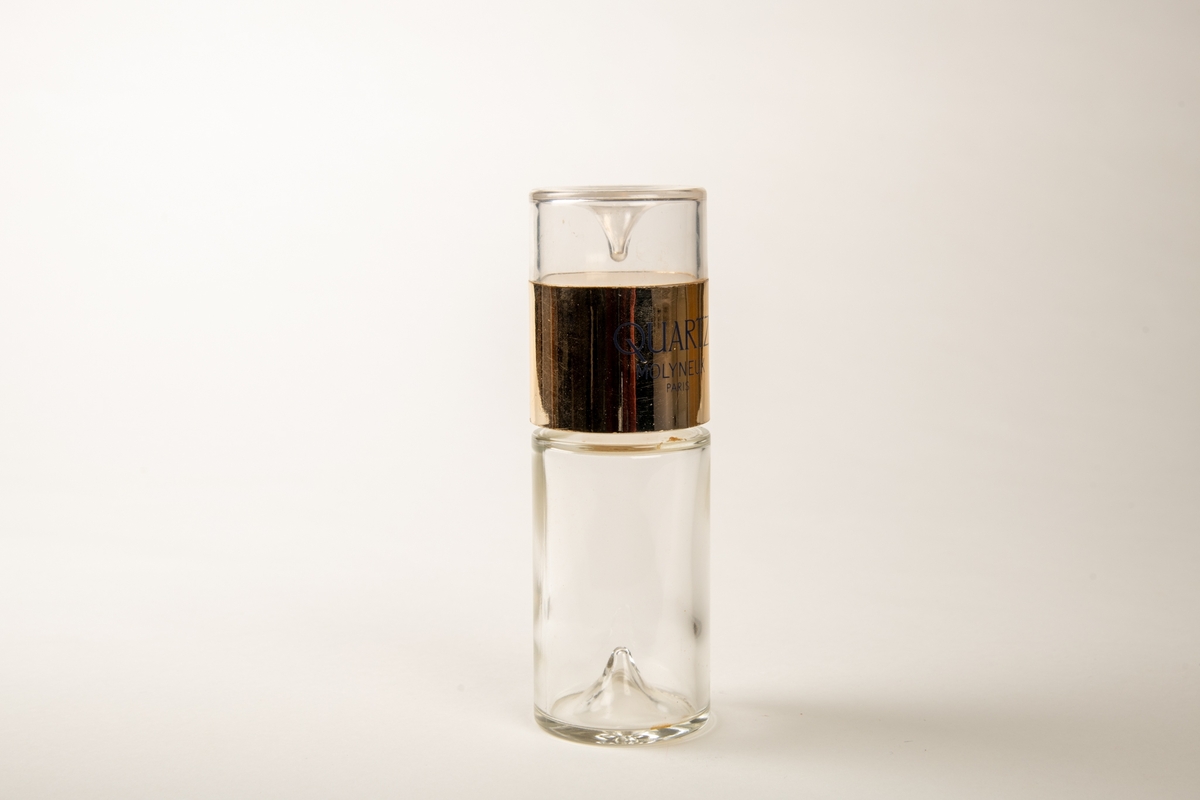 Sylindrisk flaske av tykt glass, med en oppstående dråpeform i bunnen og innv. i lokket.  Lokket er øvre del av sylinderen og har tekst:   EAU DE PARFUM 850 og QUARTZ MOLYNEUX Paris