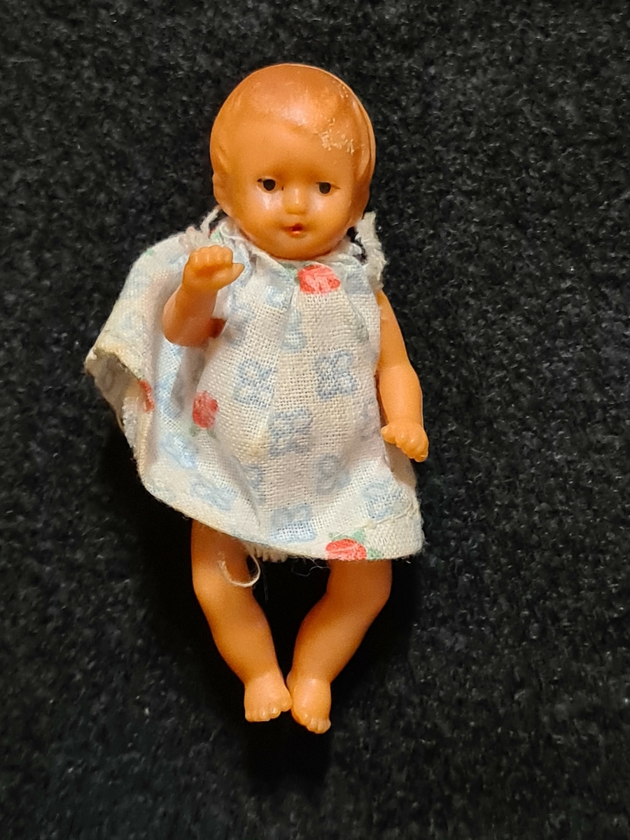 Ingår i en samling om 3 dockor och dockskåp VM17246.

1. docka, plast, utan kläder
2. docka plast med vit- blå klänning
3. docka helt i tyg med virkade kläder, röd grön