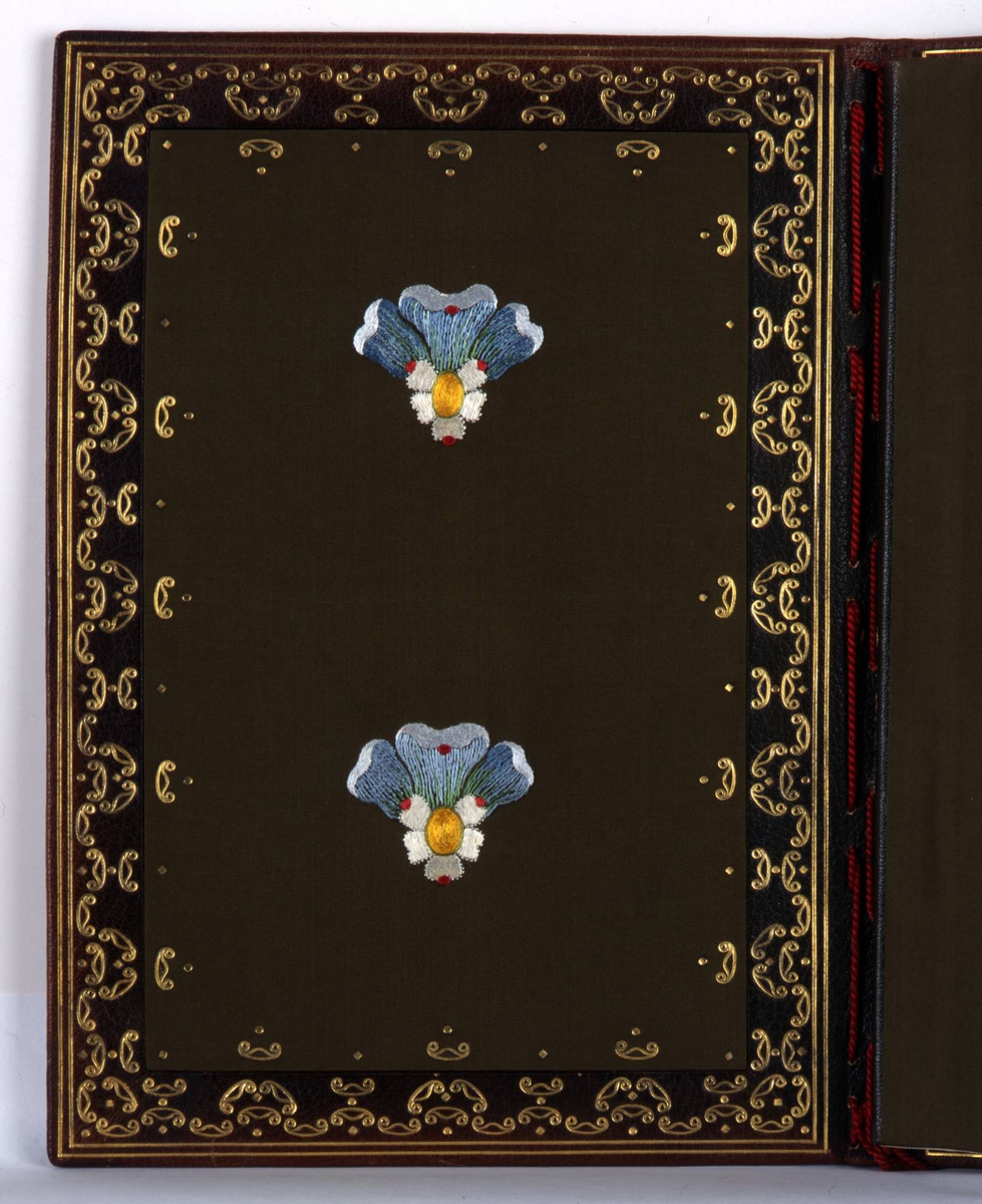 Adresse innbundet i brunt skinn med preget dekor i olivengrønt og rødt. Rød tvinnet snor i ryggen med dusker. På innsiden grønn silke med gullborder og broderte blomster.