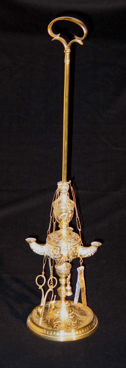 Romersk lampe i bronse (ifølge prot.) med fire armer. Fire redsaper er festet til lampen i kjetting: klype, krok, saks og slukker. Akantusmønster.