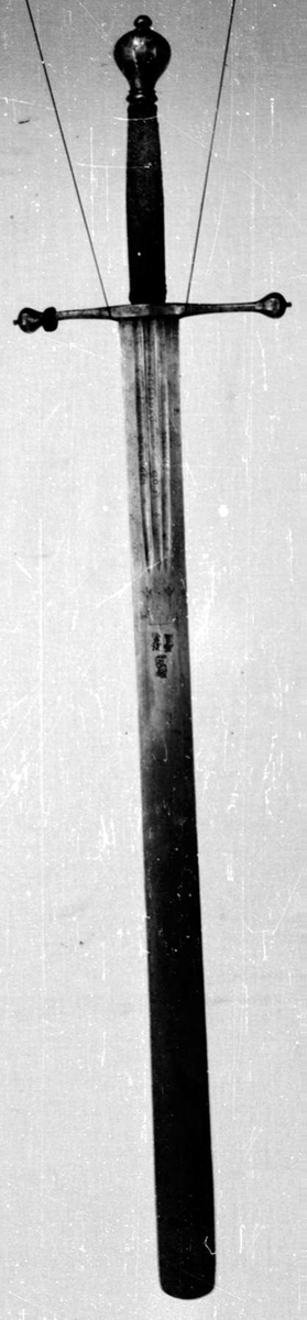 Skarprettersverd.  Pæreformet knapp med fasettetert dekor.
Tregrep viklet med rokkeskinn. 
Rette åttekantede parérstenger som ender i to dråper med kantet dekor. Rett tveegget klinge med ovalt tverrsnitt  og tre korte blodrender på hver side. Innslått tre smedstempler med kronede hoder.  På den ene siden er det gravert inn et hjul og på den andre siden en galge. Begge inngraveringer er innlagt med kobber.

