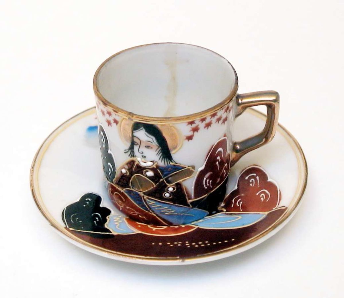 Mokkakopp med skål av hvit porselen. Både kopp og skål har håndmalt dekor. Motivet er japansk. Kanten på koppen og skålen er forgylt, likeså hanken. Koppen er limt.