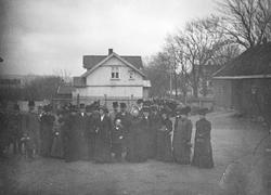 Oppstilt gruppe med mørkkledde mennesker. Mulig begravelse?