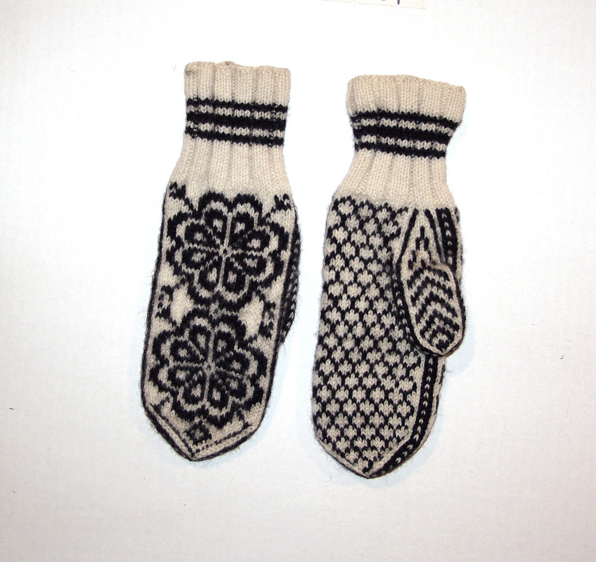 1 par strikkede votter i ull med mønster i svart og hvitt.

