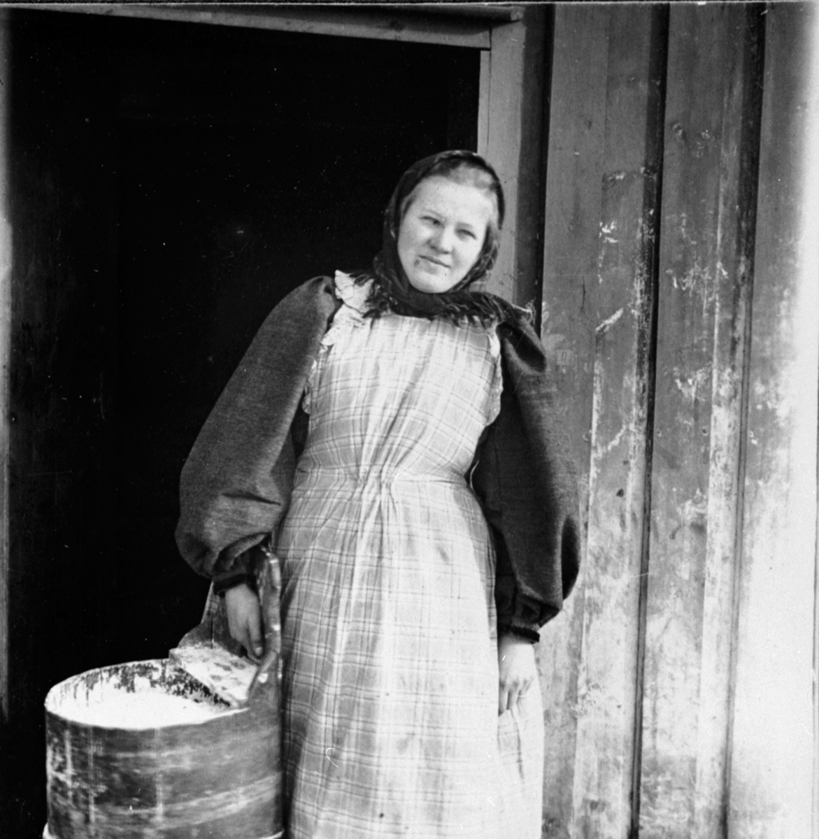 Mimi Løken f.1876 i fjøsdøra på Løken østre, Veldre, Ringsaker. I budeieklær med mjølbutt.