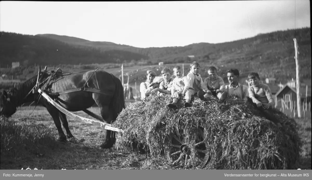 Menn og barn i gruppebilde fra høyslåtte med hest. Landskap i bakgrunn. 1931