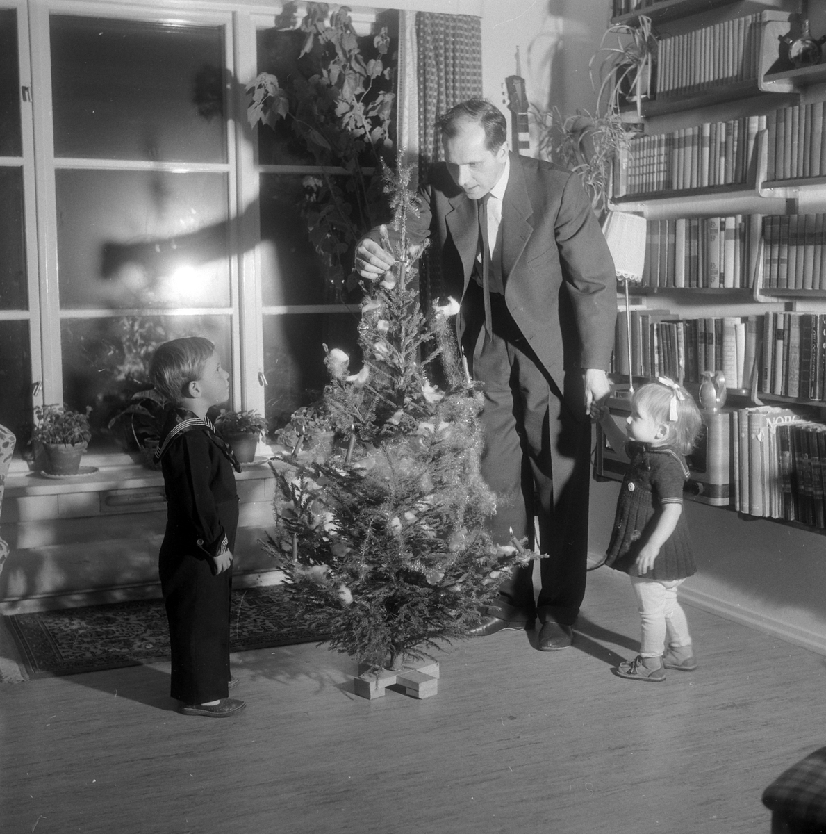 En far og to barn tenner levende lys på juletreet. Pyntet juletre.