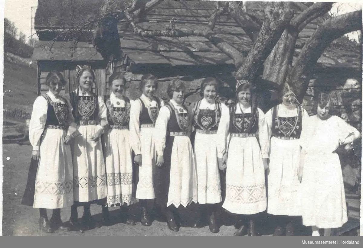 8 kvinner i bunad og ei i kvit kjole.