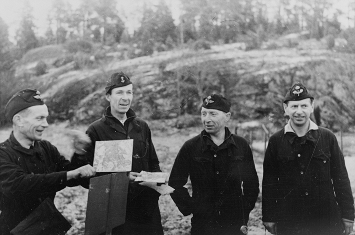 Tre män från Flygvapnet och en man från marinen står med kartor vid en skylt i terräng.
