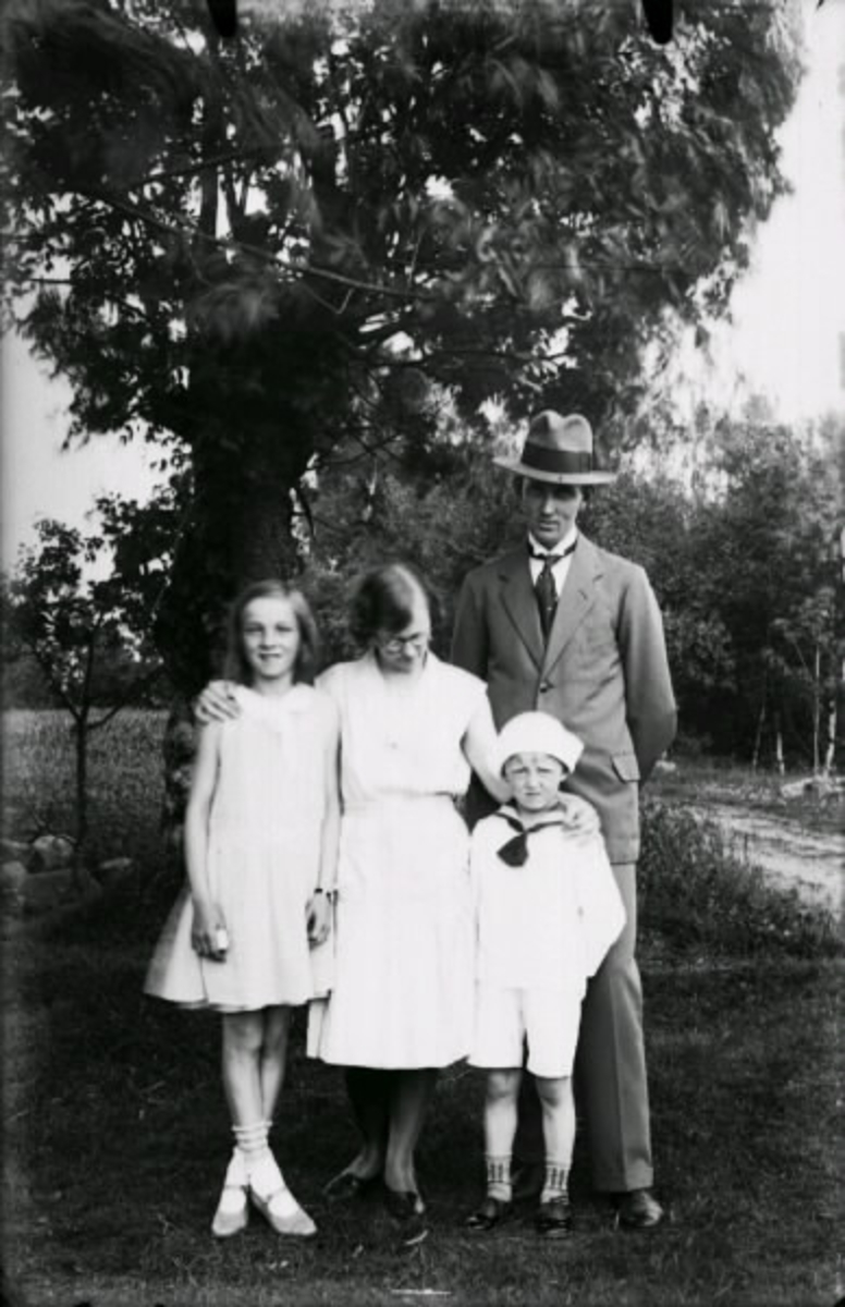 En man och en kvinna stående framför ett träd tillsammans med två barn. Pojken är Ivar Larsson, Kinnared.