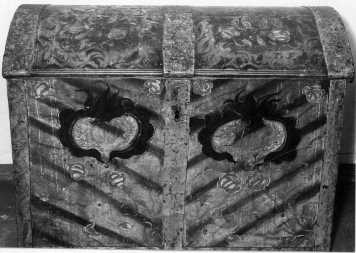 Kiste med buet lokk og smijernsbeslag og bånd. Rosemalt lokk og tre sider. Innvendig rosemaling delvis vasket bort.