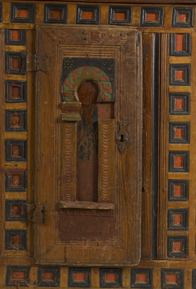 Skap i to deler. Høy skjenkebord, lav overdel. Skåret dekor i gesims med dragehoder i konsollene. Kassetter med rammefyllinger som dekor i frontpanelene. På dørene er det også malte motiv innen romanske buer. På høyre dør malte bygninger, på venstre dør er motivet uleselig. Ådret på sidene.