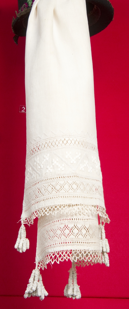 Hvit belteklut i lin med dekor av broderi og dusker.