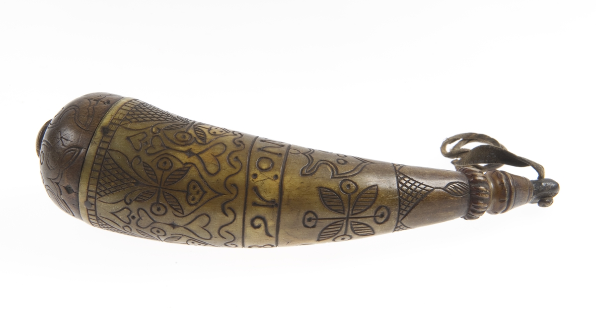 Krutthorn med skålformet bunn i tre. Plugg som er festet med et lærbånd ved hornet. Skåret dekor på horn og bunn i form av blomster, blader og hjerter.