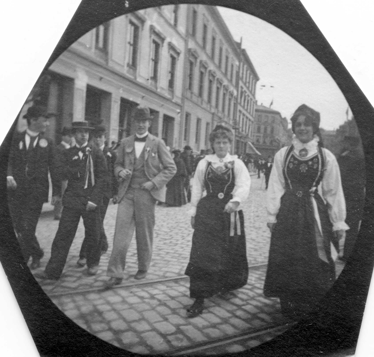 17. mai, Oslo. Fire gutter med 17.mai sløyfer og to jenter med bunad fremst i bildet.