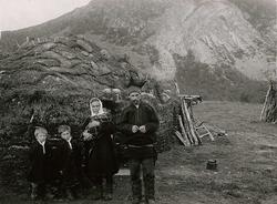 Familiegruppe (5) i samisk drakt, oppstilt foran gamme ved S
