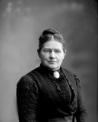 Portrett, kvinne i svart kjole, brosje i halsen. Fru H P Fay