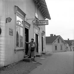 Fevik, Grimstad, april 1957. Kvinne foran pensjonat.