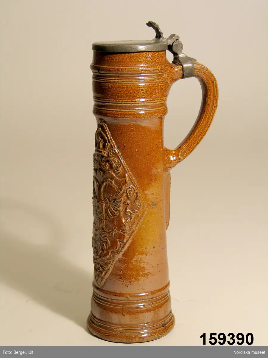 Krus av brunt saltglaserat stengods, så kallad "Schnelle", daterat 1583. Lock av tenn. Tillverkat i Raeren, Tyskland (numera Belgien).
Tegnér 2006