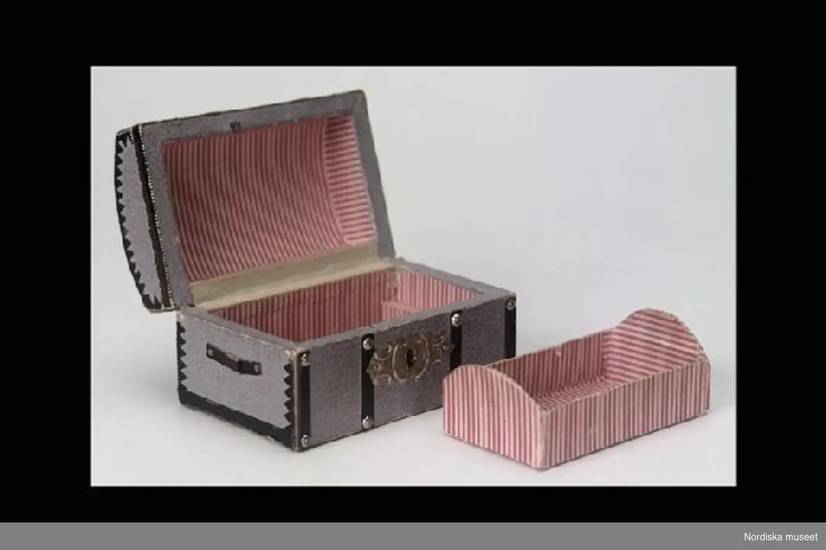 Inventering Sesam 1996-1999:
a) L 10,5 cm, B 6,5 cm, H 6,5 cm
b) L 8,5 cm
a) Koffert av trä, klädd med grått papper imiterande läder. Dekorerad med svarta läderband och metallstift i rutmönster. Kupigt lock med textilt gångjärn. Nyckelskylt av vitmetallplåt (nyckel saknas) Inuti klädd med 
b) insats till kofferten. Klädd med röd och vitrandigt papper.
Har tillhört fröken Siri Rhodin (1849-1949) och har ev. använts som leksak av henne. Ursprungligen var kofferten troligen en chokladask. Dylika askar användes av chokladtillverkaren "Suchard", Neuch¿tel, Schweiz. Jmfr inv.nr. 165.261
Bilaga
Leif Wallin feb 1997