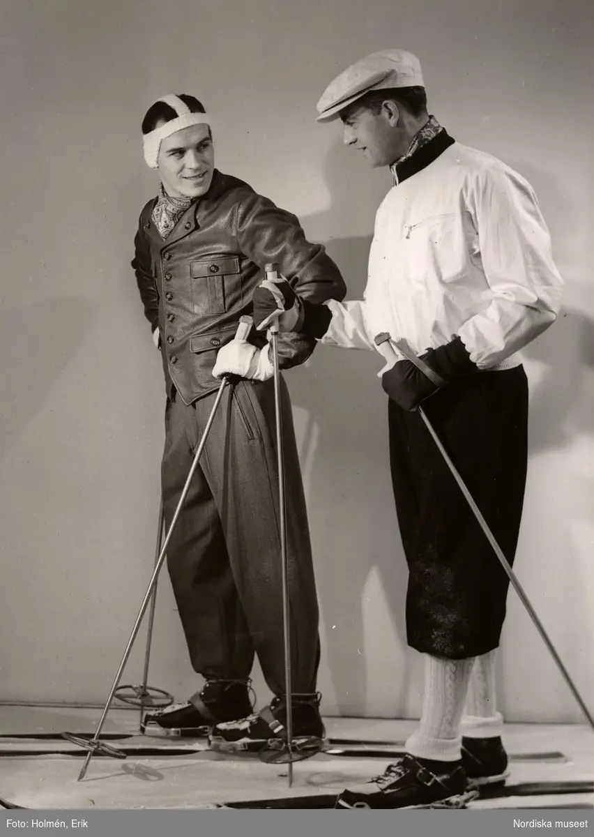 Sportkläder, herrkonfektion på Nordiska Kompaniet 1944. Två män i skidkläder står bredvid varandra med skidor på fötterna och stavar i händerna.