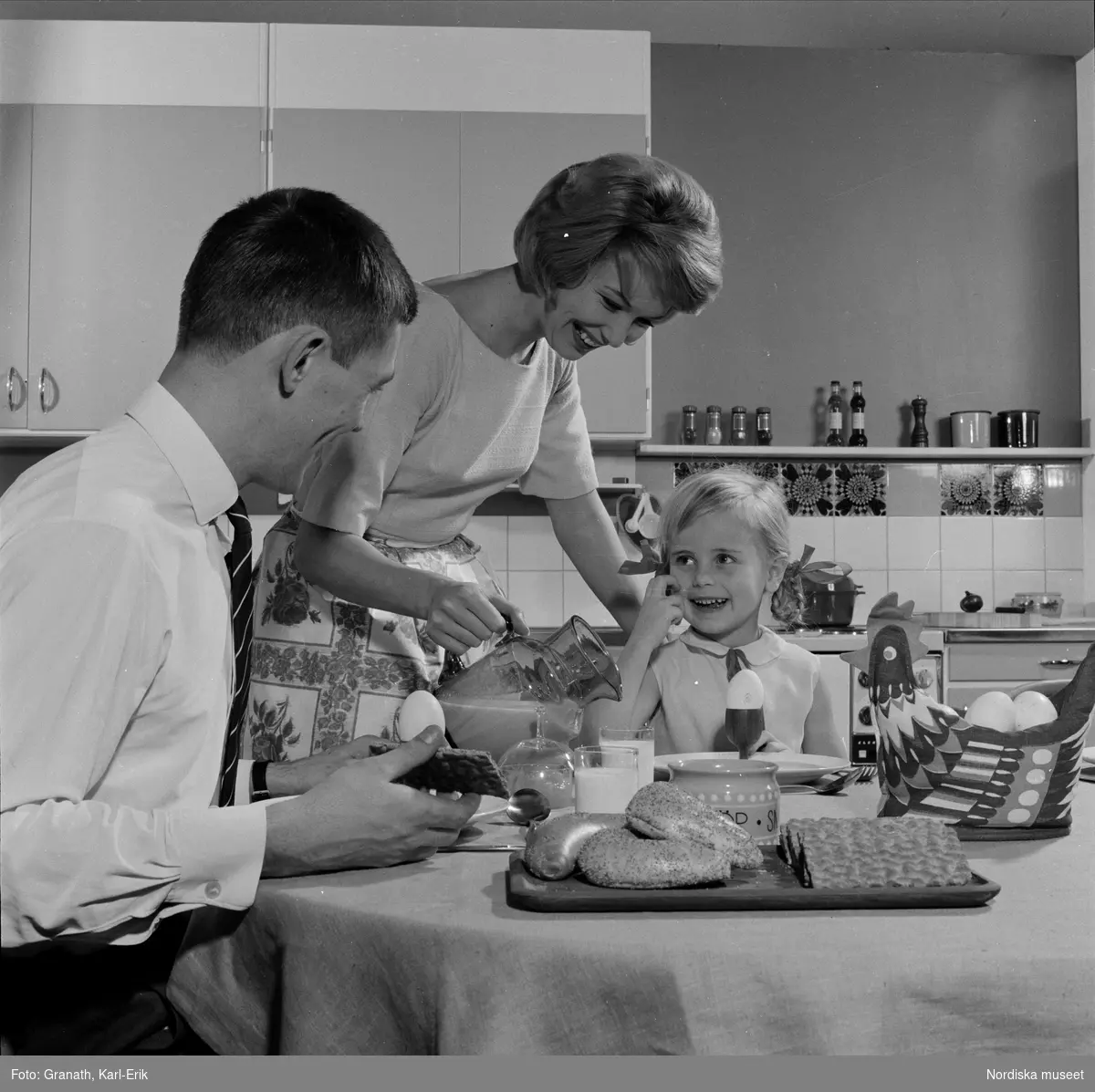Familj vid dukat bord. Man, kvinna och liten flicka i kök äter frukost.